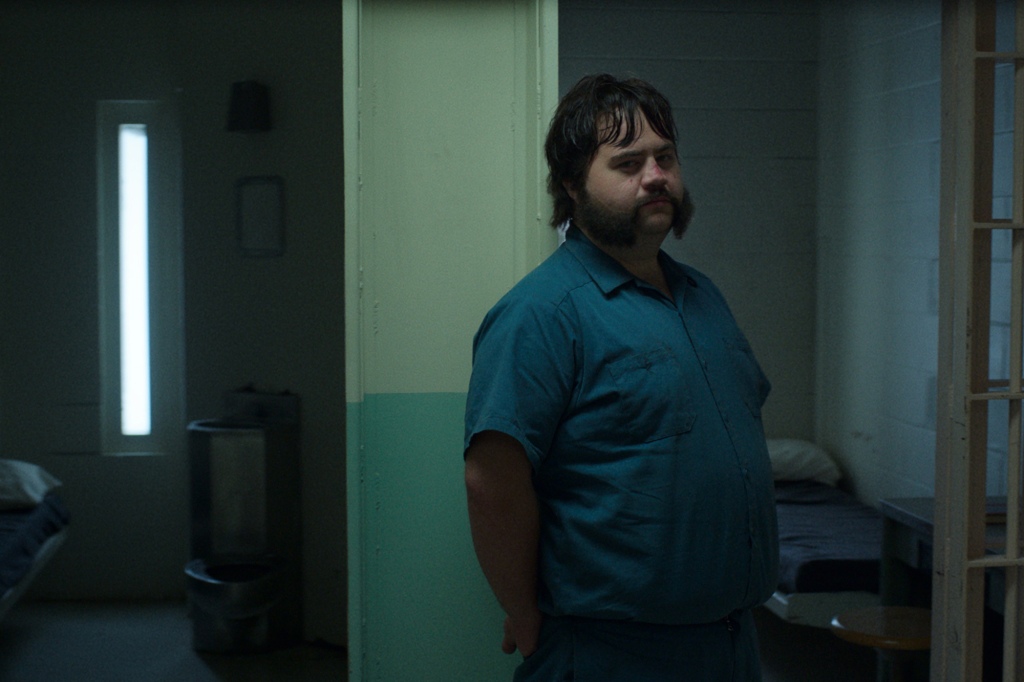 Larry Hall (Paul Walter Hauser) stares out from his prison cell in a scene from "Black Bird." He's wearing a blue prison jumpsuit and has several red marks on his face.