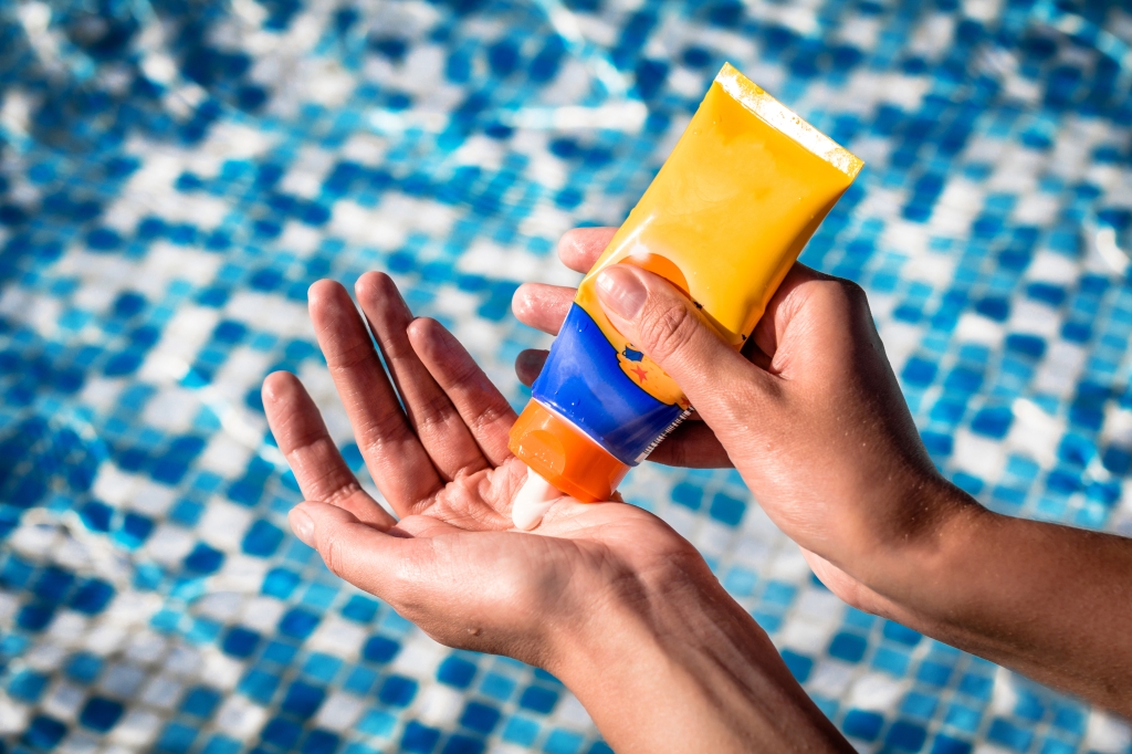 A woman squeezes sunscreen out a tube and into her hand.