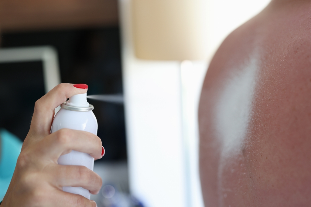 A woman sprays sunscreen on a man's back.