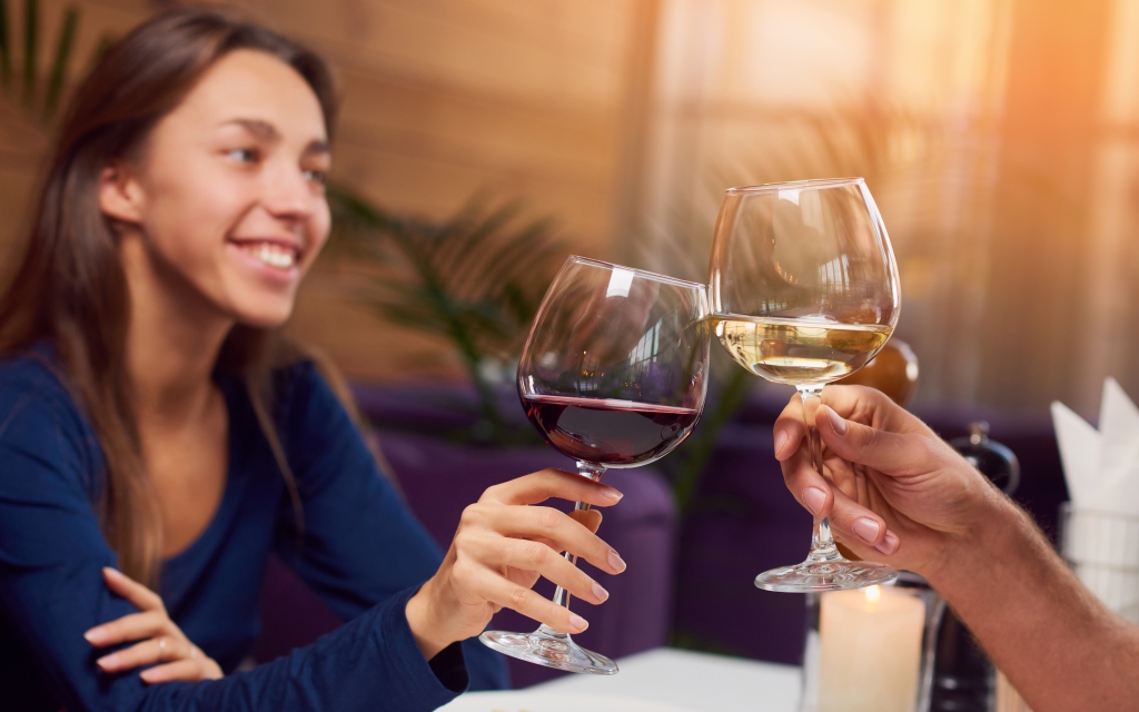 A woman toasts her red wine with an unseen white wine dinker.