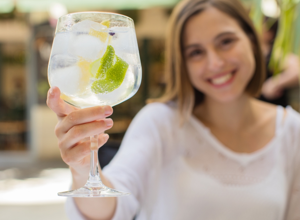 A woman holds a gin and tonic while smiling.