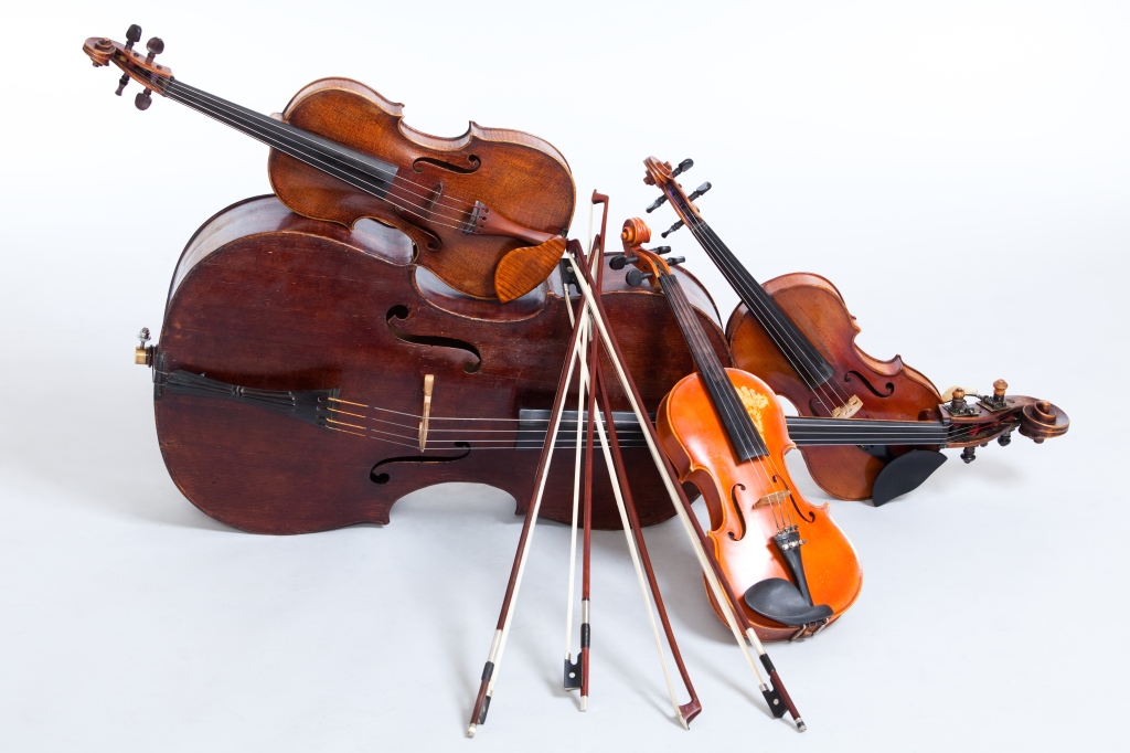 A pile of string instruments lie propped up against one another.