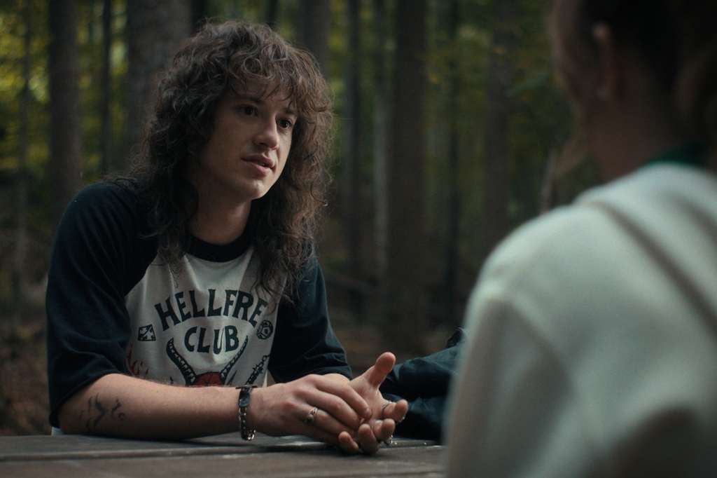 Eddie (Joseph Quinn) sits at a table in the woods. 