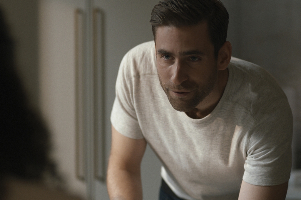 Oliver Jackson-Cohen in “Surface,” leans across a table looking intense. 