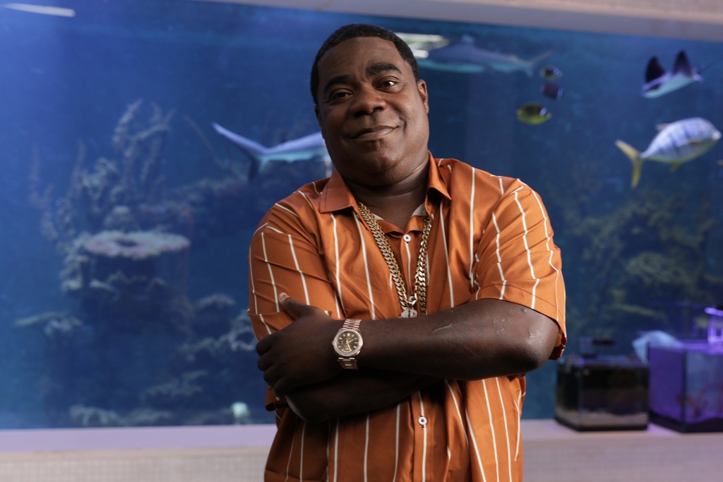 Photo of Tracy Morgan. He's smiling and looking at the camera and is wearing an orange shirt with white stripes. He's got his arms folded on his chest.