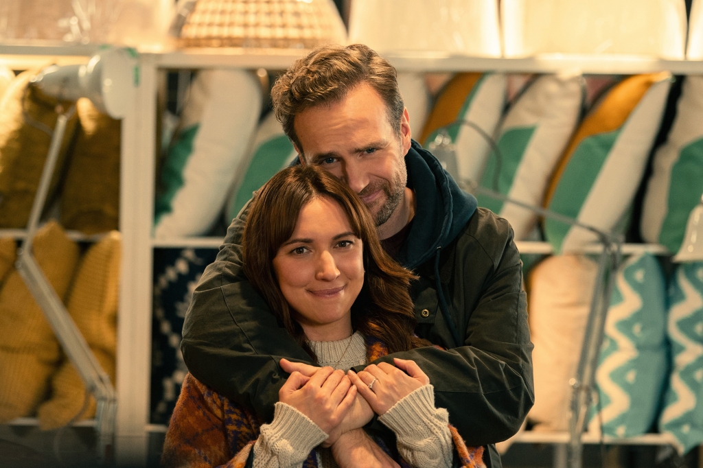 Esther Smith and Rafe Spall as Nikki and Jason. Jason has his arms around around Nikki and they're both facing the camera and smiling. She's holding his arms.