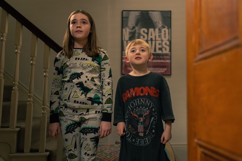 Photo of Eden Togwell and Mike McAnulty as Princess and Tyler. She's wearing pajamas with dinosaurs on them and Tyler is wearing Jason's Ramones T-shirt, which is down to his knees. They're standing on the staircase and looking toward the camera.