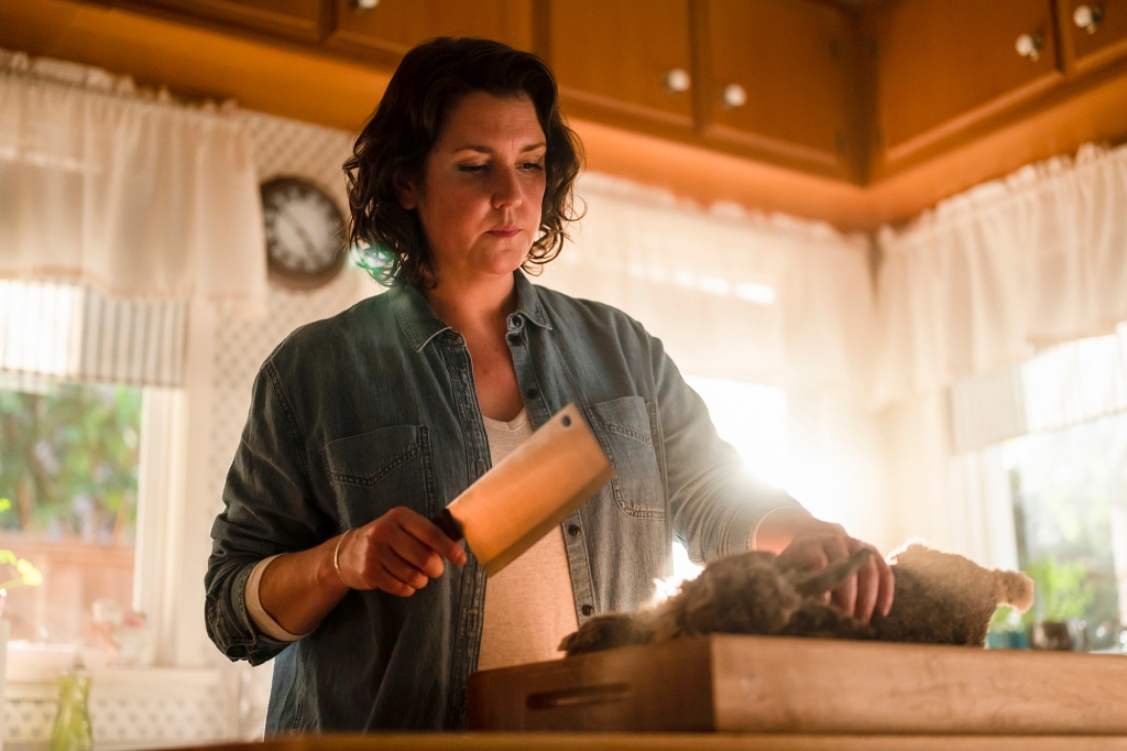 Melanie Lynskey in the Showtime series "Yellowjackets." She's in the kitchen and holding a butcher's knife and is standing over a cutting board with what looks like a dead rabbit lying on it.