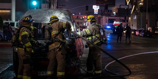 Firefighters work at the scene of a burnt collective transport vehicle after it was set on fire by unidentified individuals in Tijuana, Baja California state, Mexico, on August 12, 2022. 