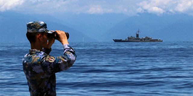 In this photo provided by China’s Xinhua News Agency, a People's Liberation Army member looks through binoculars during military exercises as Taiwan’s frigate Lan Yang is seen at the rear.