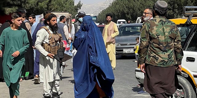 Taliban forces block roads around an airport, while a woman with a Burqa walks by in Kabul, Afghanistan, Aug. 27, 2021. 