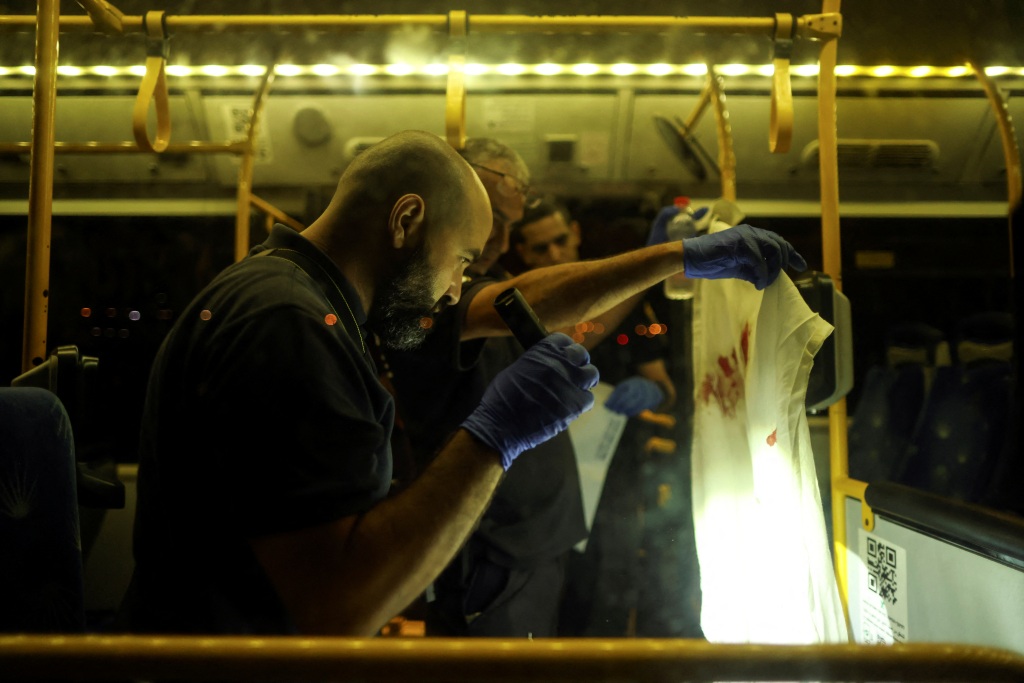An Israeli police officer checks a bloodstained cloth on a bus following the incident in Jerusalem on August 14, 2022. 