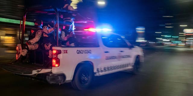 Armed members of the National Guard drive past the site of a burnt collective transport vehicle after it was set on fire by unidentified individuals in Tijuana, Baja California state, Mexico, on August 12, 2022.