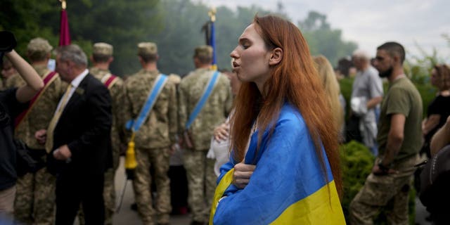 A woman wrapped in a Ukrainian flag attends the funeral of activist and soldier Roman Ratushnyi in Kyiv, Ukraine, June 18, 2022.