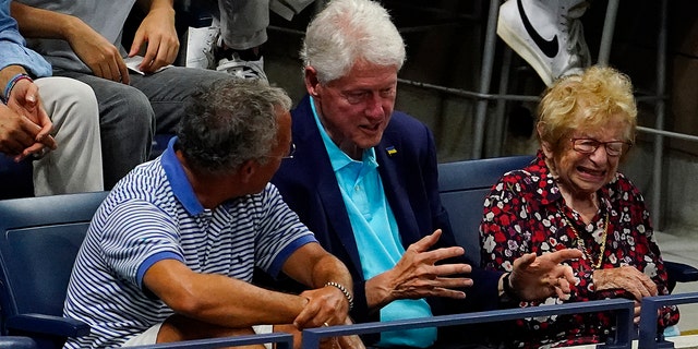 Former President Bill Clinton, center, and Ruth Westheimer, right, sit together during the first round of the US Open tennis championships, Monday, Aug. 29, 2022, in New York.