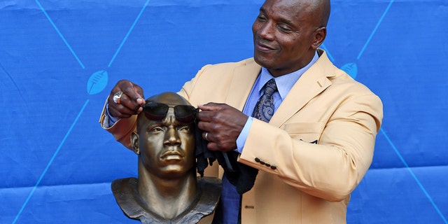 Former NFL player Bryant Young playfully puts some shades on his bust during an induction ceremony at the Pro Football Hall of Fame in Canton, Ohio, Saturday, Aug. 6, 2022.