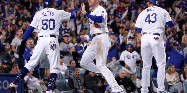 Los Angeles Dodgers' Freddie Freeman, center, is congratulated by Mookie Betts, left, and Edwin Rios after they scored on a double by Trea Turner during the fourth inning of a baseball game against the Atlanta Braves Monday, April 18, 2022, in Los Angeles.