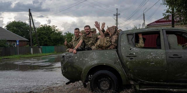 TOPSHOT - Ukranian soldiers wave from the back of a pick-up as they drive to the frontline during a rainy day in the city of Sloviansk, eastern Ukraine, on August 2, 2022, amid the Russian invasion of Ukraine. 