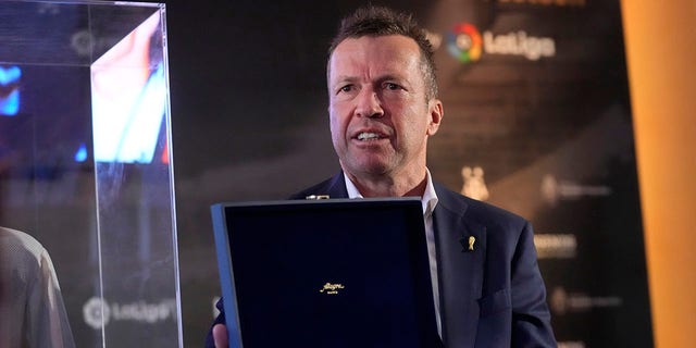 Former German soccer player Lothar Matthaus holds an award he was given by the Argentina embassy in recognition of his football career and contribution of sporting values after donating  the shirt worn by Diego Armando Maradona in the final of the 1986 World Cup in Mexico, during an event at the Argentine Embassy in Madrid, Spain, Thursday Aug. 25, 2022. The shirt was given to Matthaus, after he exchanged shirts with Maradona at the end of the final match. Matthaus has donated the shirt to the Legends football museum in Madrid. 