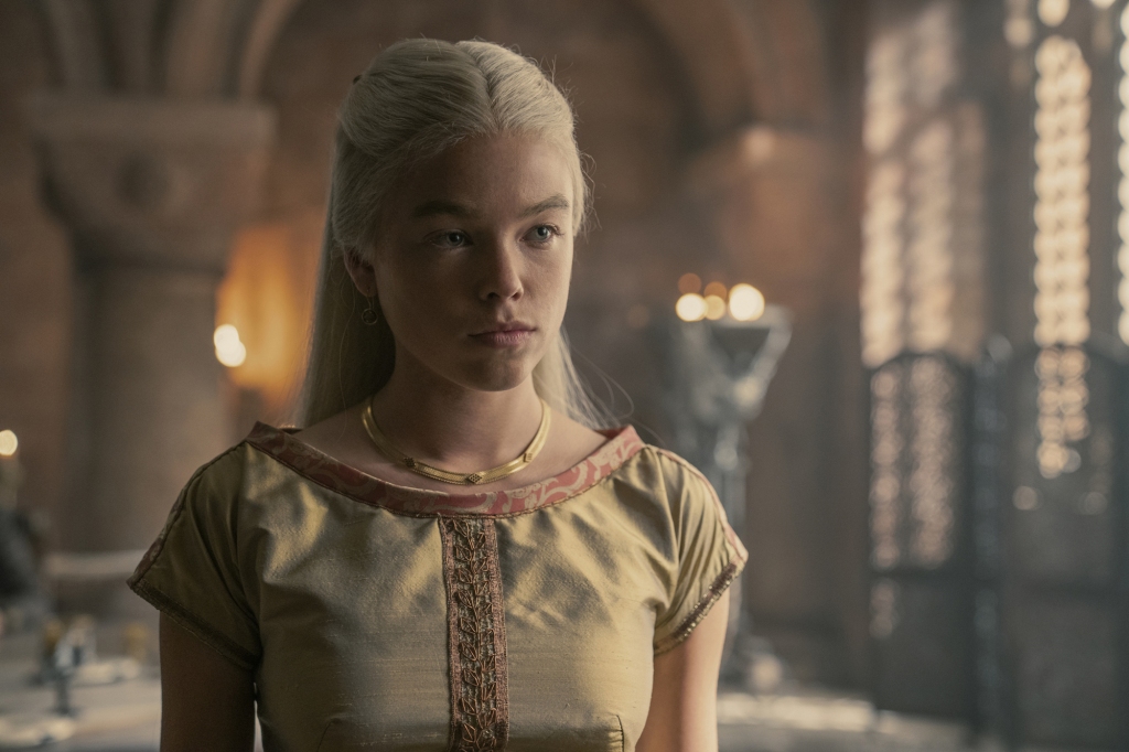 Milly Alcock as Princess Rhaenyra Targaryen in "House of the Dragon" standing in a room wearing a dress. 