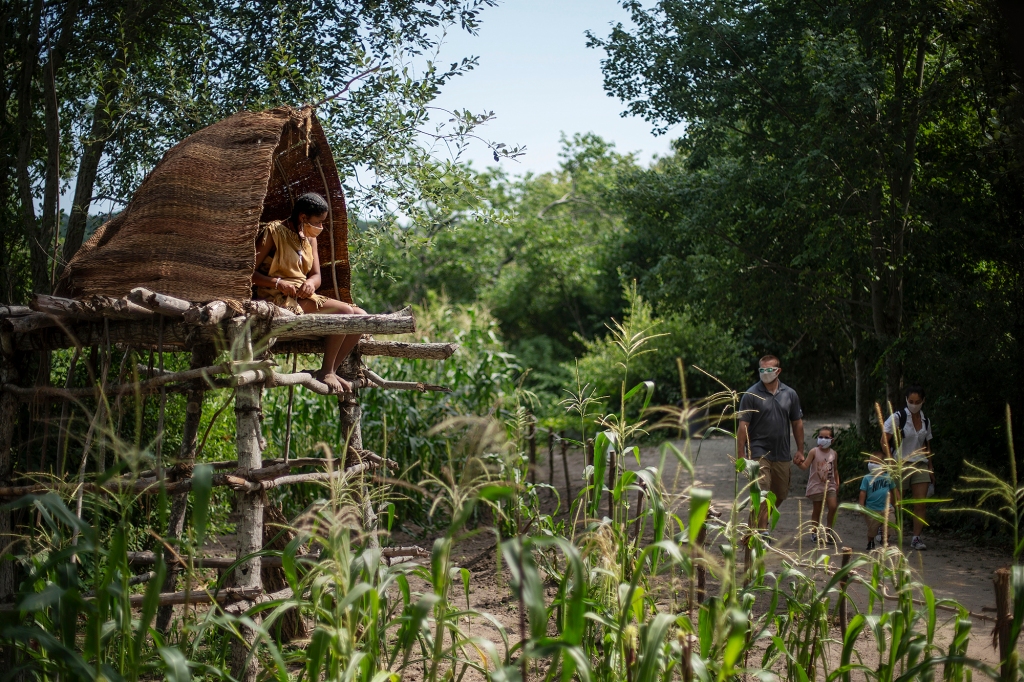 Alyssa Harris, a member of the Mashpee Wampanoags and a museum educator at Plimoth Patuxet Museums sits in a corn watch tower as visitors walk through the Wampanoag Homesite living history exhibit. Former museum staffers say museum officials for years ignored their suggestions for modernizing and expanding the outdoor exhibit.