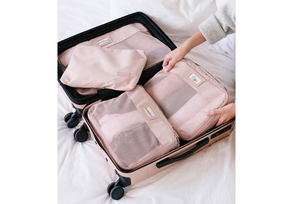 Hands place pink packing cubes into an open suitcase
