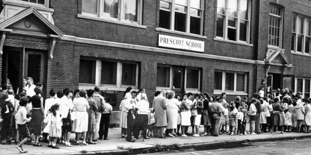 FILE - Parents and their children wait in long lines outside a Syracuse school to receive the Sabin oral polio vaccine on Aug. 29, 1961. 