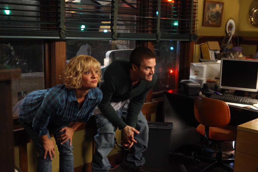 Photo of Martha Plimpton and Garret Dillahunt in a scene from their old Fox sitcom, "Raising Hope." They're both bending over and making funny faces in an office setting.