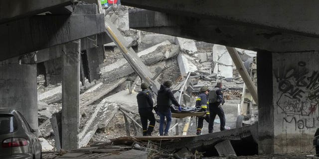 Ukrainian soldiers carry a body of a civilian killed by the Russian forces under the destroyed bridge in Irpin close to Kyiv, Ukraine, Thursday, March 31, 2022.