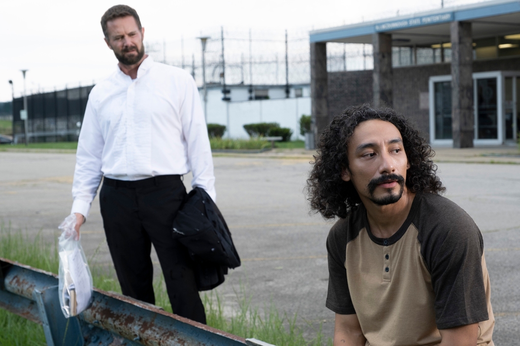 Photo of Garret Dillahunt and Phillip Garcia as Jack and Rooster. They're sitting outside of the prison after being freed; Jack is wearing a white buttoned-down short; Rooster has a goatee and curly hair and is wearing a two-toned brown short-sleeve shirt.