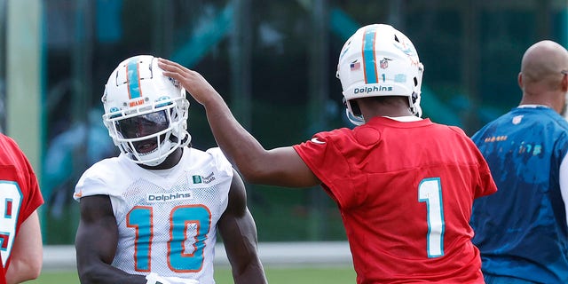 Tua Tagovailoa #1 taps the helmet of Tyreek Hill #10 of the Miami Dolphins between drills during the Miami Dolphins Mandatory Minicamp at the Baptist Health Training Complex on June 1, 2022 in Miami Gardens, Florida.