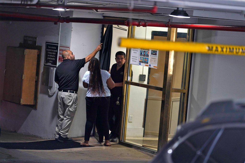 Three people stand at the doorway from a parking garage to a building.
