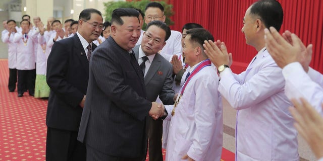 In this photo provided by the North Korean government, North Korean leader Kim Jong Un shakes hands with a health official in Pyongyang, North Korea, Wednesday, Aug. 10, 2022. 