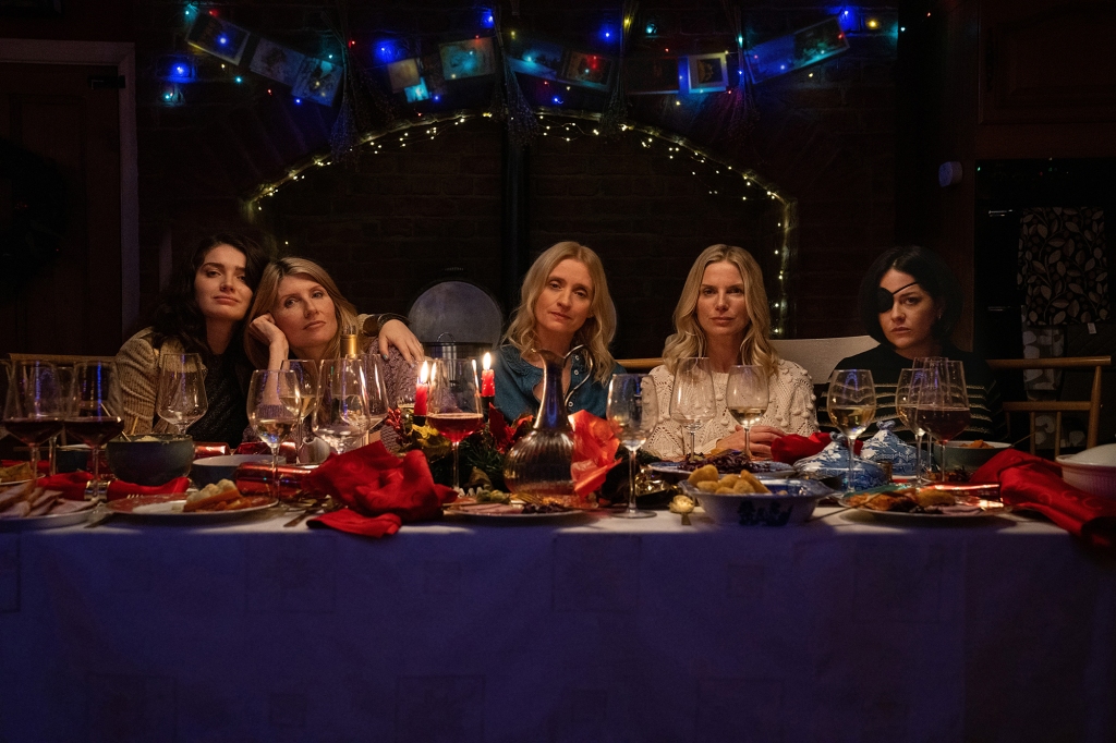 The Garvey sisters sitting in a line at a table at night looking at the camera: Becka (Eve Hewson), Eva (Sharon Horgan), Grace (Anne-Marie Duff), Ursula (Eva Birthistle) and Bibi (Sarah Greene) in “Bad Sisters." 