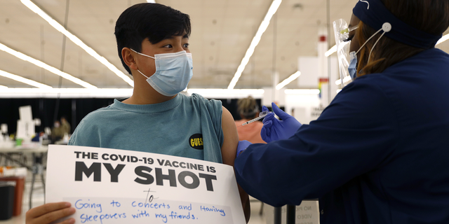 Lucas Kittikamron-Mora, 13, holds a sign in support of COVID-19 vaccinations as he receives his first Pfizer vaccination at the Cook County Public Health Department on May 13 in Des Plaines, Ill. 