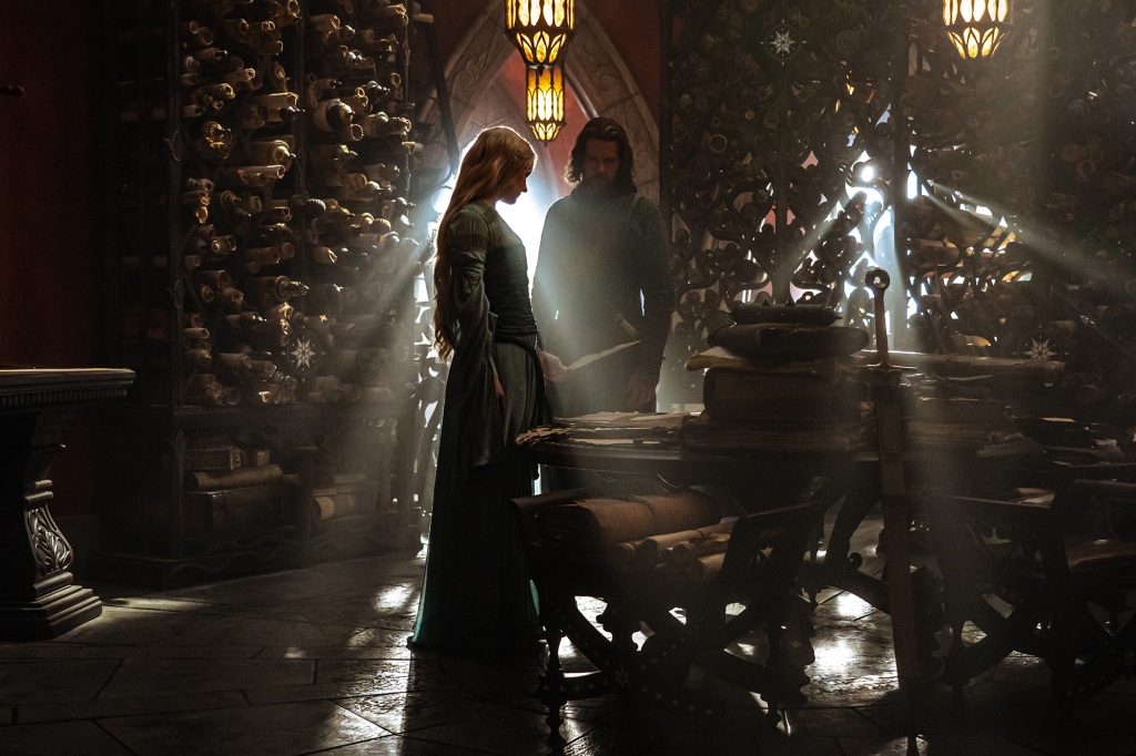 Galadriel (Morfydd Clark) with Elendil (Lloyd Owen) standing in a dim room looking at a book in "The Rings of Power." 