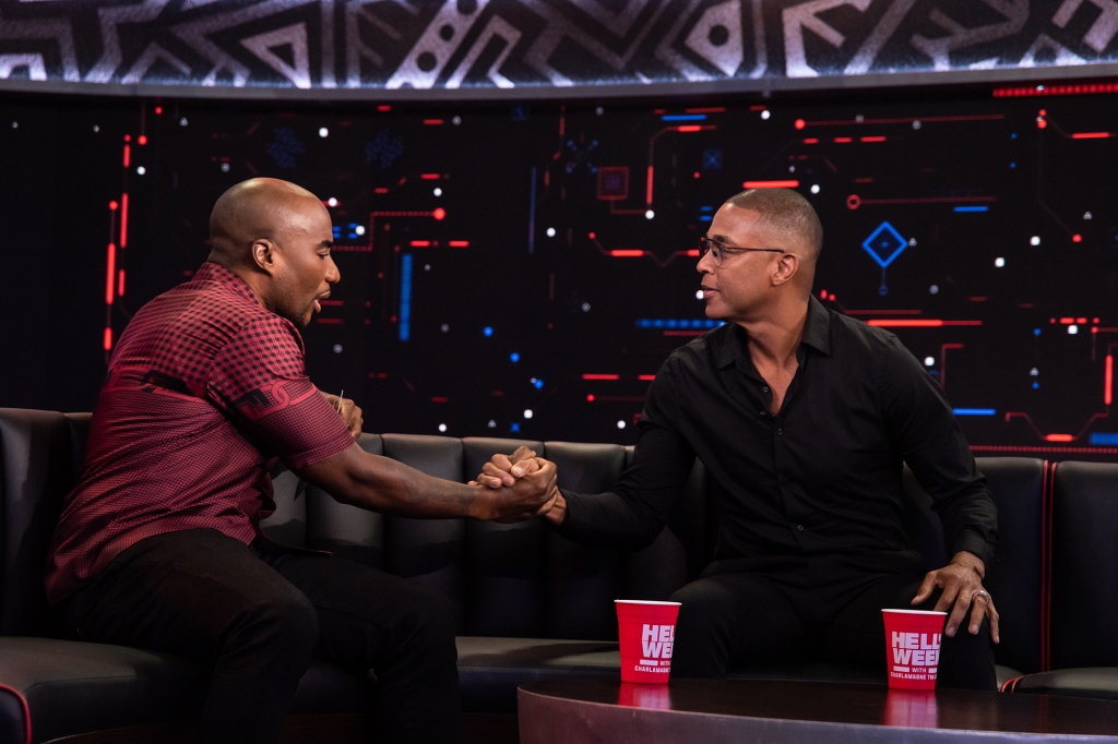 Charlamagne Tha God clasps hands with guest Don Lemon on a recent episode of "Hell of A Week with Charlamagne Tha God." They're sitting on a couch facing each other; Charlamage is wearing a red shirt and Don is wearing a black shirt.