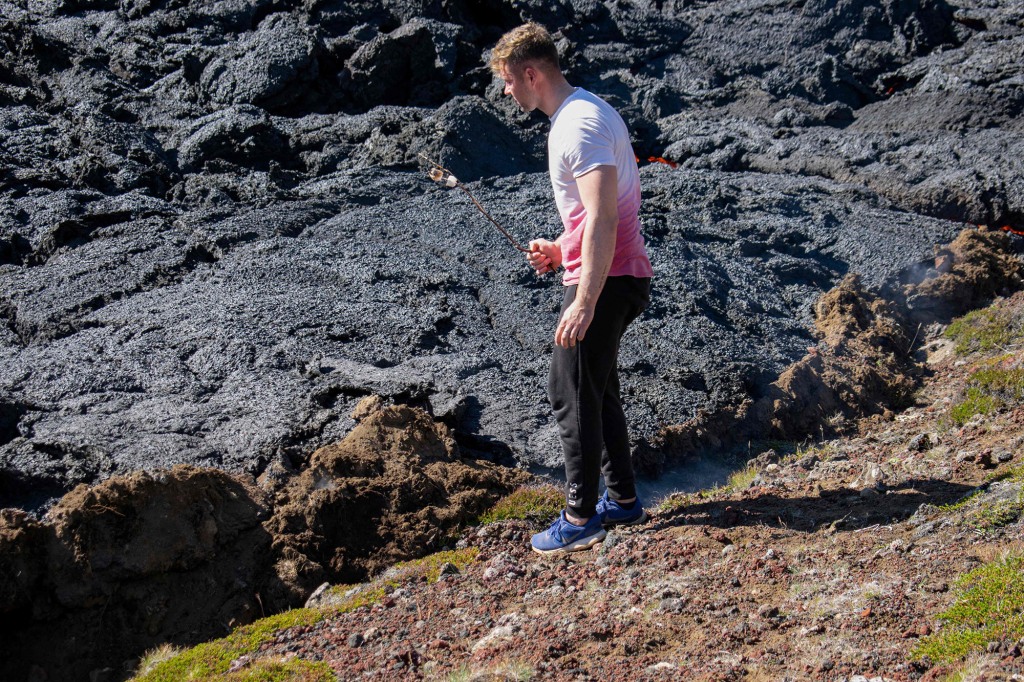 A man heats food on a stick on the scene of the newly erupted volcano taking place in Meradalir valley, near mount Fagradalsfjall, Iceland on August 4, 2022.