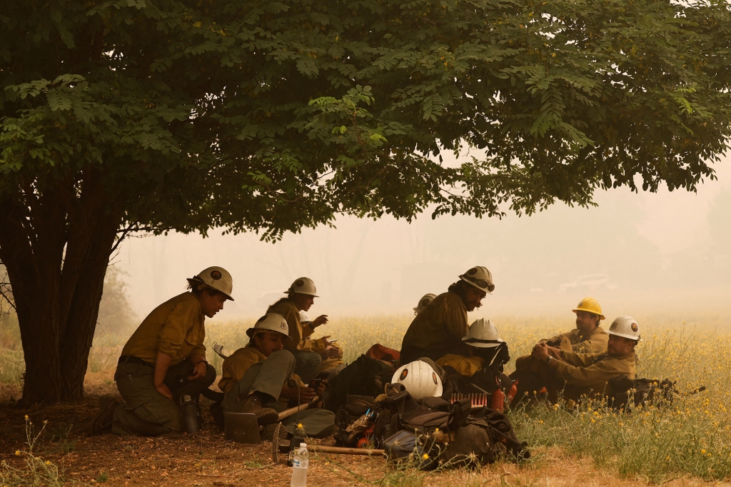 Firefighters rest under a tree