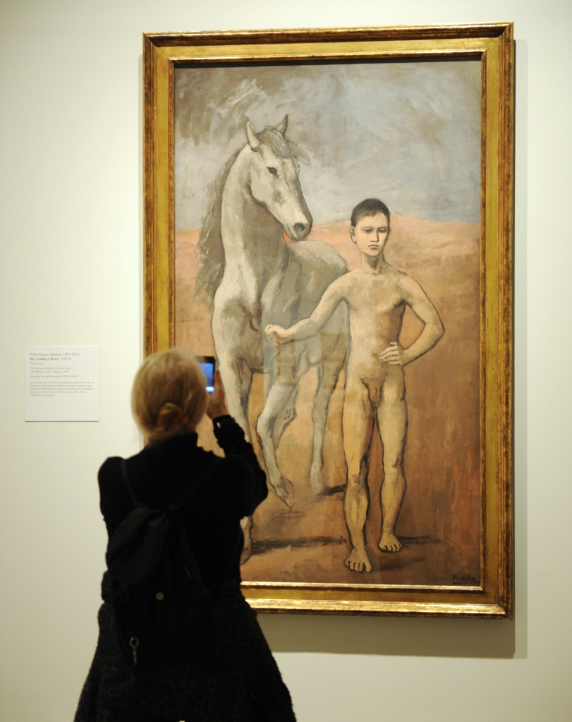 A woman takes a cellphone photograph of "Boy Leading a Horse" 1905-06 by Pablo Picasso.
