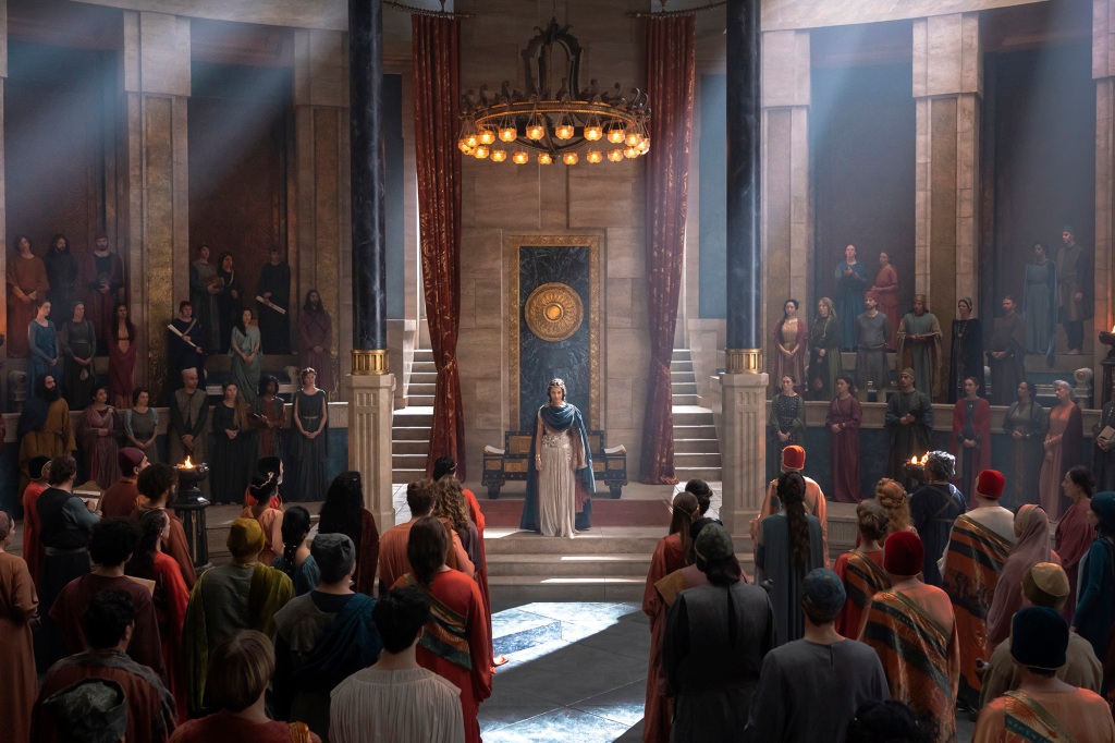 Queen Regent Míriel (Cynthia Addai-Robinson) stands in the middle of an ornate room surrounded by a crowd. 