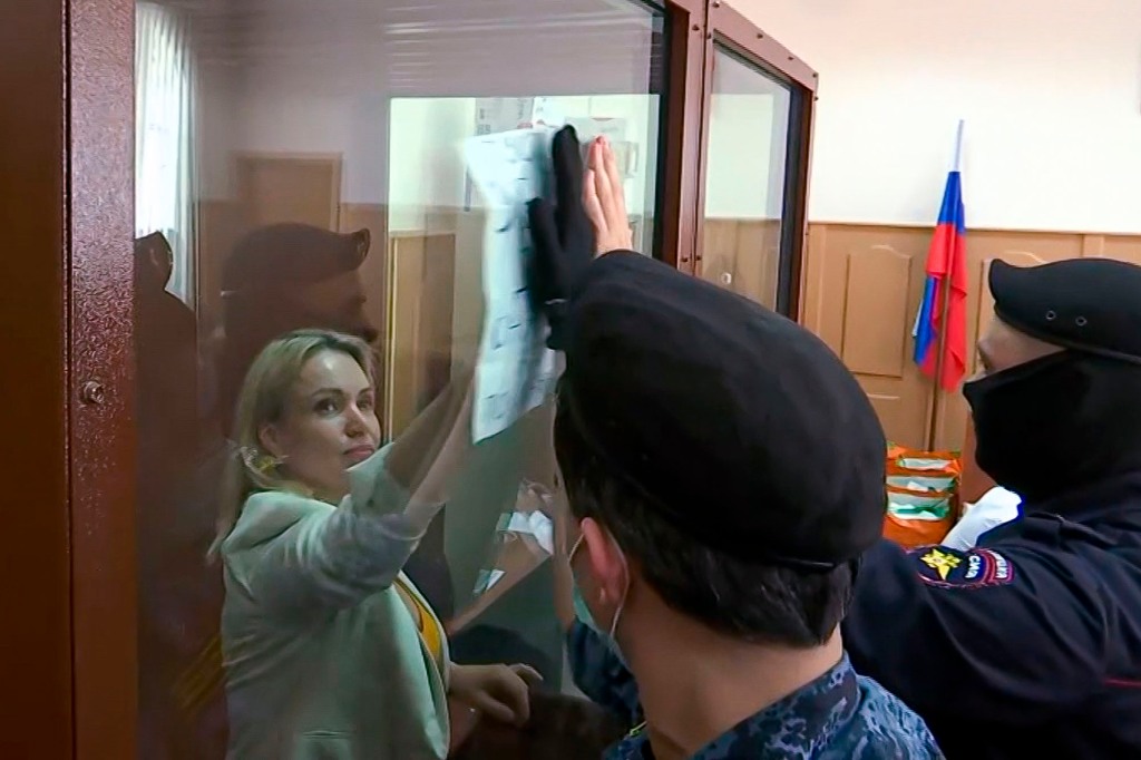In this photo taken from video Marina Ovsyannikova, a former Russian state TV journalist who quit after making an on-air protest of Russia's military operation in Ukraine, holds up a poster that says "Let the murdered children come to you in your dreams at night" through a cage glass as police officers try to cover the poster with their hands at a court room prior to a hearing in Moscow, Russia, Thursday, Aug. 11, 2022