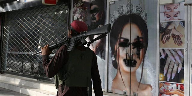 A Taliban fighter walks past a beauty salon with images of women defaced using spray paint in Shar-e-Naw in Kabul on August 18, 2021. 