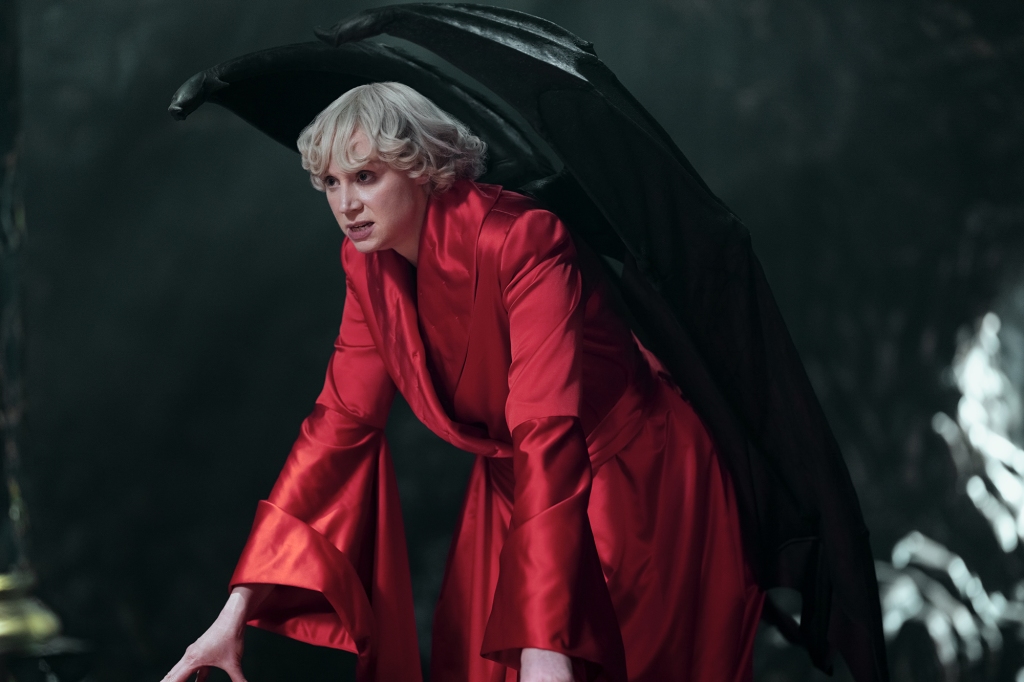 Gwendoline Christie as Lucifer in "The Sandman" leans over a table in a red robe. 