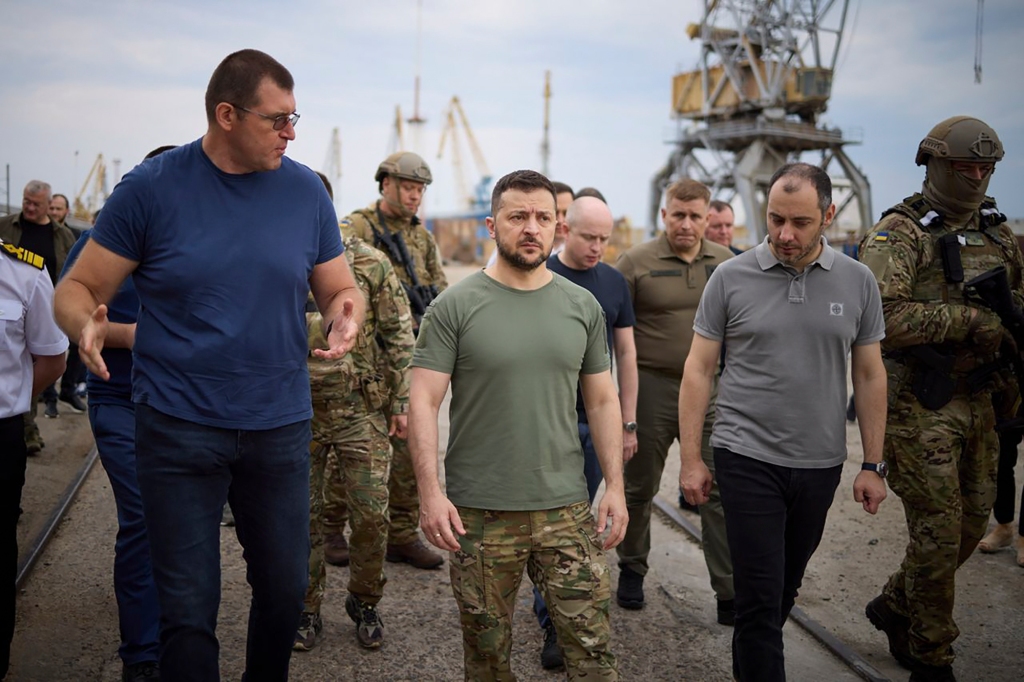 In this photo provided by the Ukrainian Presidential Press Office, Ukrainian President Volodymyr Zelenskyy, center, surrounded by ambassadors of different countries and UN officials, visits a port in Chornomork during loading of grain on a Turkish ship, background, close to Odesa, Ukraine, Friday, July 29, 2022.
