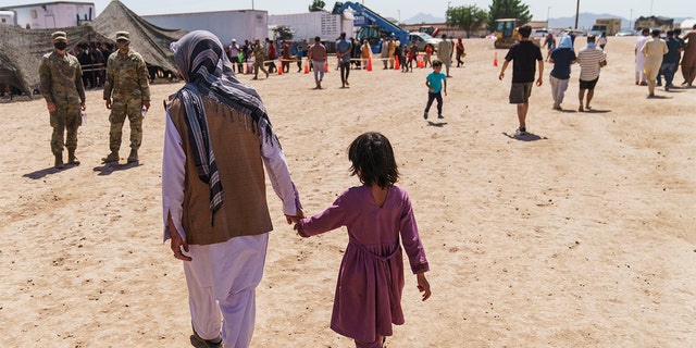 A man walks with a child through a military base in New Mexico where Afghan refugees are being housed.