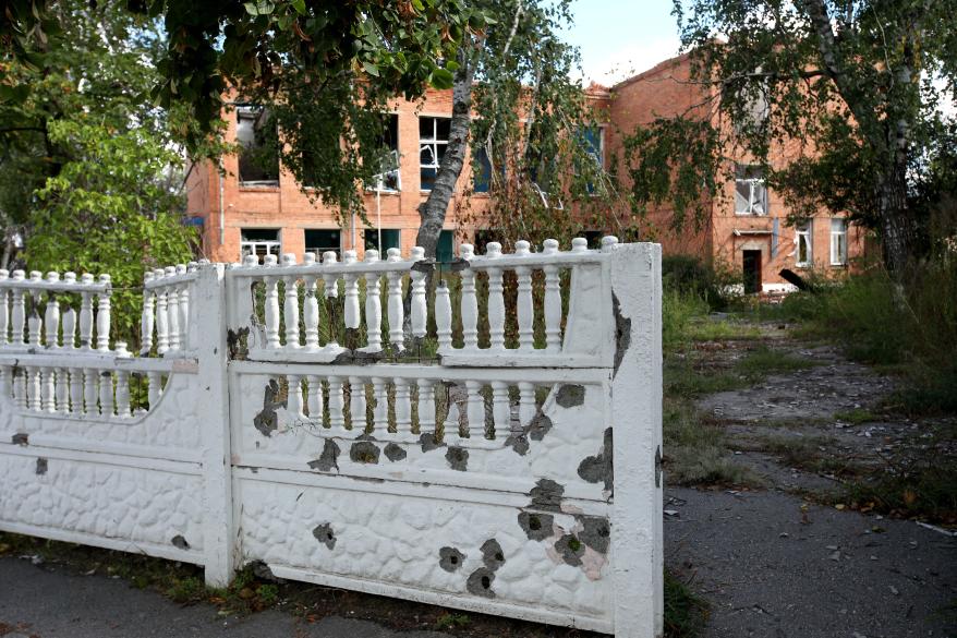 Holes are spotted on a fence outside a school that was destroyed in a Russian shelling near Izium Ukraine.