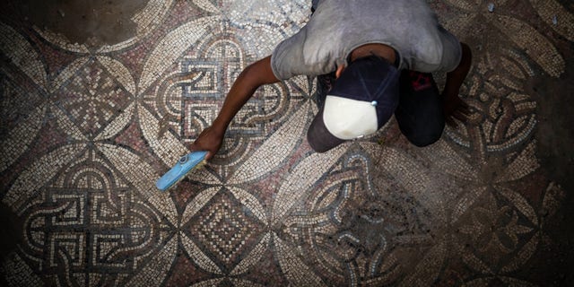 A Palestinian sweeps dust off parts of a Byzantine-era mosaic floor that was uncovered by a farmer in Bureij in central Gaza Strip, Sept. 5, 2022. 