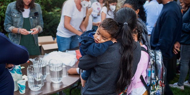 A woman, who is part of a group of immigrants that had just arrived, holds a child as they are fed outside St. Andrews Episcopal Church, Wednesday Sept. 14, 2022, in Edgartown, Mass., on Martha's Vineyard.