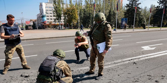 Investigators work at the site of a burning vehicle after shelling in Donetsk, area controlled by Russian-backed separatist forces, eastern Ukraine, Saturday, Sept. 17, 2022. A Ukrainian shelling attack killed four people in downtown Donetsk on Saturday. According to the city's Mayor Alexey Kulemzin, fragments of munitions for Caesar howitzers were found.